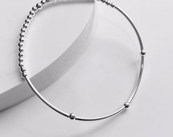 Puede incluir: Un brazalete de plata con un diseño de cuentas. El brazalete tiene tres cuentas más grandes espaciadas uniformemente alrededor del brazalete.