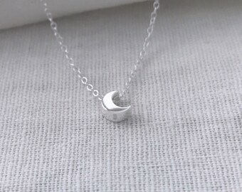 May include: A delicate silver necklace with a small crescent moon pendant.