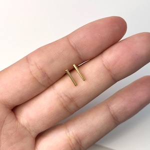 May include: A pair of gold bar stud earrings. The earrings are simple and minimalist, and they are perfect for everyday wear.