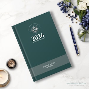 Può includere: Un'agenda aziendale e personale 2026 color teal con la scritta "Purpose Action Success". L'agenda ha un logo a forma di bussola e una fascia grigia nella parte inferiore. Sono visibili anche una penna blu e una candela.