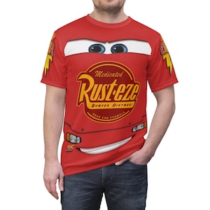 May include: Red t-shirt with a cartoon image of a red race car with blue eyes and a smile. The car has a yellow and black logo that says "Medicated Rusteze Bumper Ointment Rear End Formula".
