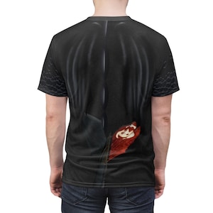 May include: Black t-shirt featuring a detailed graphic design. The design appears to be a stylized representation of a dragon's wing and a red, clawed hand. The shirt has a crew neck and short sleeves. The sleeves have a scale-like pattern.