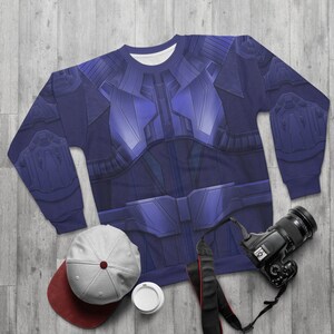 Puede incluir: Una sudadera azul con un diseño futurista impreso en la parte delantera. El diseño presenta una armadura azul metálica con formas geométricas y un cinturón.