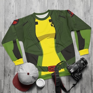 May include: Green and yellow long-sleeved sweatshirt with a cartoon character design. The character is wearing a green jacket and yellow shirt with a red X on the belt.