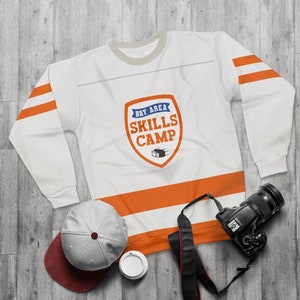 May include: White sweatshirt with orange and blue stripes. The sweatshirt has a logo on the front that says "Bay Area Skills Camp" with a hockey puck graphic.