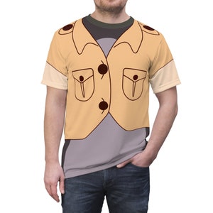 Puede incluir: Una camiseta de manga corta con un diseño de dibujos animados de una chaqueta color beige con botones y bolsillos marrones oscuros. La camiseta tiene una combinación de colores gris y verde oscuro, con el diseño de la chaqueta impreso en la parte delantera.