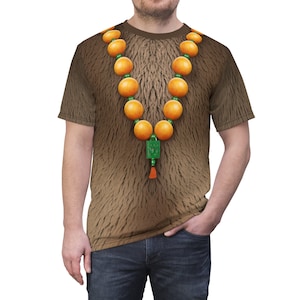 Puede incluir: Una camiseta marr&oacute;n con textura de pelo y un collar de cuentas naranjas con un dije verde.