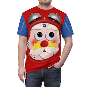 May include: A red t-shirt featuring a whimsical clock face design. The clock face has a red frame, a white mustache, and a yellow band. The sleeves are blue. The clock shows the number 12. The shirt is worn by a person.