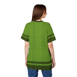 K&ouml;nnte beinhalten: Ein gr&uuml;nes T-Shirt in Strickoptik mit kurzen &Auml;rmeln und einem dunkelgr&uuml;nen Kragen. Das Shirt hat dunkelgr&uuml;ne Streifen an den &Auml;rmeln und am Saum. Das Shirt wird von einer Person getragen, die von der Kamera abgewandt ist.