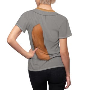 Könnte beinhalten: Graues kurzärmeliges T-Shirt mit vertikaler Rippstruktur und braunem Kragen. Auf der Rückseite des Shirts befindet sich ein großes, flauschiges, orange-braunes Fuchsschwanz-Design. Die Person trägt eine schwarze Jeans.