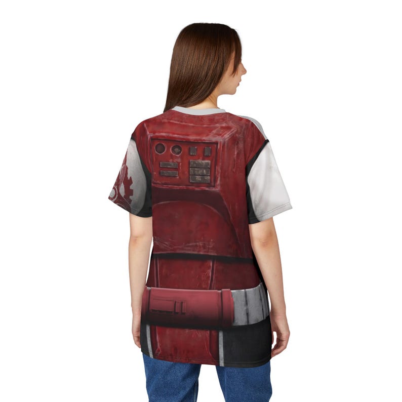 May include: A red and white t-shirt with a detailed armour design. The design includes rectangular panels, buttons, and a belt, with a weathered appearance. The sleeves are white. The shirt is worn by a person.