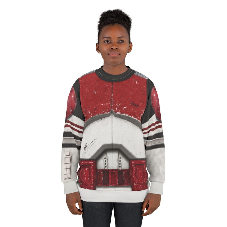 May include: A crew neck sweatshirt with a design in red, white, and grey, resembling a military uniform. The long-sleeved top has a detailed graphic print across the chest and shoulders.