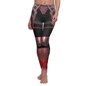 May include: Black leggings with a red and copper-colored armor design. The leggings feature a high waist and a detailed print resembling protective gear, with red accents and a geometric pattern.