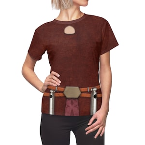 May include: A brown t-shirt with a keyhole neckline and a printed design resembling a belt with metallic accents. The shirt has short sleeves and a textured appearance, creating a unique visual effect.