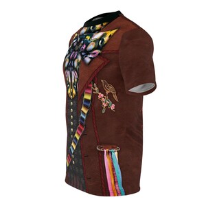Puede incluir: Una camiseta marr&oacute;n con un dise&ntilde;o estampado que se asemeja a un chaleco. El dise&ntilde;o del chaleco incluye una mariposa colorida, un p&aacute;jaro en una rama y una cinta a rayas. La camiseta tiene cuello negro y mangas cortas.