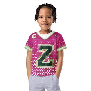May include: A magenta and white dotted jersey-style t-shirt with a large green and black letter "Z" on the front. The shirt has a white collar and green and white striped sleeves. A small "C" is on the left shoulder.