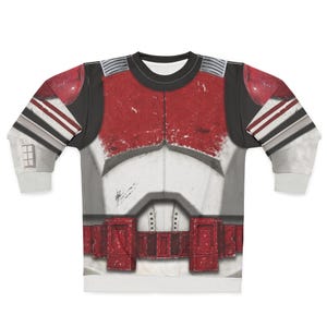 May include: A long-sleeved sweatshirt with a detailed print of a red, white, and grey battle suit. The design includes a chest plate, shoulder pads, and a belt, with distressed textures for a realistic look. The sleeves have grey and white stripes.