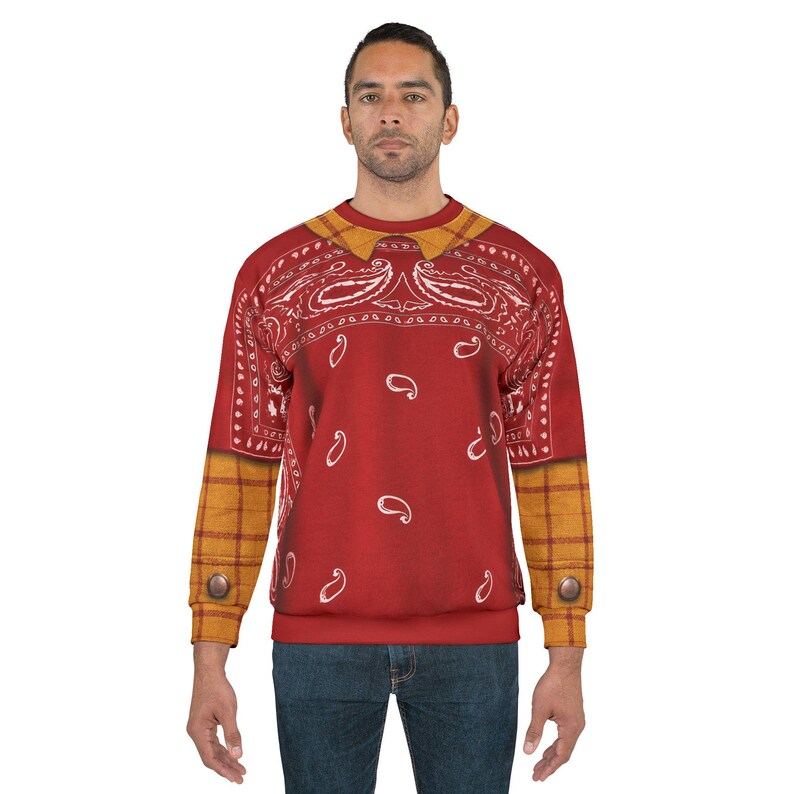 May include: A long-sleeve crewneck sweatshirt featuring a red bandana print with white paisley patterns across the chest and back. The sleeves and collar have a yellow and brown plaid pattern, with a single brown button detail on each cuff.
