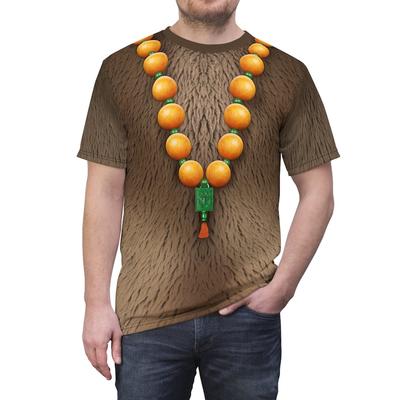 Puede incluir: Una camiseta marr&oacute;n con textura de pelo y un collar de cuentas naranjas con un dije verde.