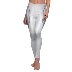 Puede incluir: Leggings blancos con un diseño plateado y dorado. Los leggings tienen una cintura alta y una silueta ajustada. Los paneles plateados recorren los lados de las piernas, con ribetes dorados que delinean los paneles plateados. Los leggings están hechos de un material liso y brillante.