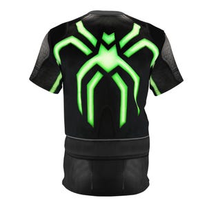Peut inclure: T-shirt noir avec un motif d'araign&eacute;e vert n&eacute;on au dos. Le t-shirt pr&eacute;sente un motif textur&eacute; sur les &eacute;paules et la partie inf&eacute;rieure. Le motif d'araign&eacute;e brille sur le tissu noir.