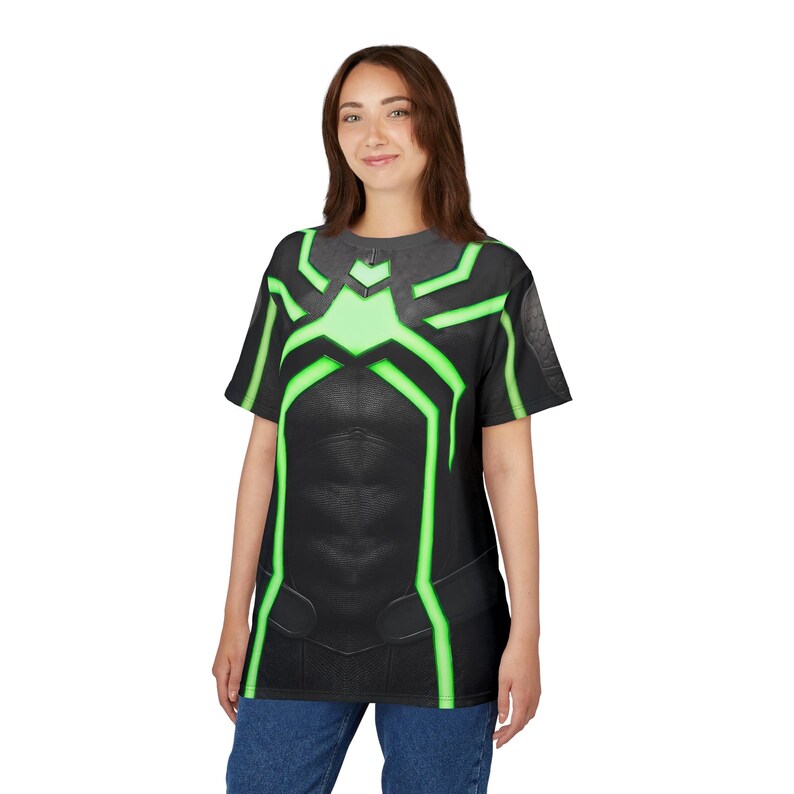 Peut inclure: T-shirt noir avec un motif vert et noir. Le t-shirt pr&eacute;sente un motif vert en forme d'araign&eacute;e sur la poitrine et les &eacute;paules. Le t-shirt est port&eacute; par une personne portant un jean bleu.