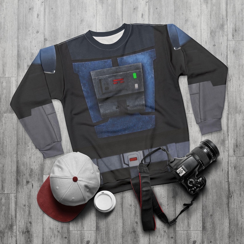 Puede incluir: Una sudadera de manga larga negra y azul con un dise&ntilde;o gr&aacute;fico, una gorra de b&eacute;isbol blanca y granate, una c&aacute;mara negra con correa y una taza de caf&eacute; blanca con tapa.