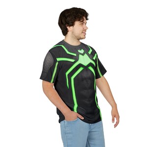 Peut inclure: T-shirt noir avec un motif de toile d'araign&eacute;e verte. Le t-shirt pr&eacute;sente un graphisme d&eacute;taill&eacute; d'un costume de super-h&eacute;ros, avec une &eacute;paulette textur&eacute;e et une plaque pectorale stylis&eacute;e. Le design est mis en valeur par des lignes vertes vives.
