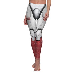 May include: White and red leggings with a graphic design. The leggings feature a white base with black and red accents, and a design that resembles armor. The lower legs are red with a distressed texture.