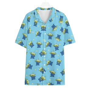 May include: A light blue short-sleeved shirt featuring a repeating pattern of green, three-eyed aliens in blue outfits and yellow stars. The shirt has a white collar and is buttoned down the front.