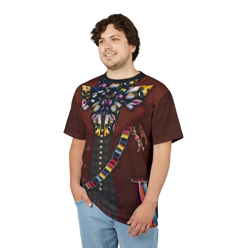 Puede incluir: Una camiseta marr&oacute;n con un dise&ntilde;o estampado de una chaqueta formal y una gran pajarita. El dise&ntilde;o de la chaqueta incluye un chaleco, una faja colorida y detalles florales. La camiseta la lleva una persona con vaqueros azules.