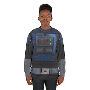 Puede incluir: Una sudadera negra y gris con un dise&ntilde;o azul y gris que se asemeja a un uniforme futurista. El dise&ntilde;o incluye un panel rectangular con detalles rojos y verdes y un dise&ntilde;o de cintur&oacute;n gris en la cintura. La sudadera la lleva una persona.