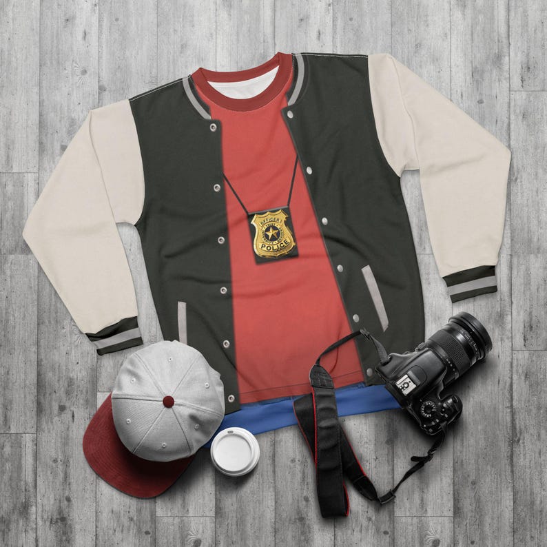 May include: A flat lay of a costume ensemble featuring a black and cream varsity jacket, a red t-shirt, a police badge, a baseball cap, a camera, and a coffee cup. The jacket has black and cream sleeves and a gray trim.