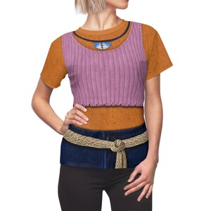 May include: A short-sleeved orange t-shirt featuring a printed design of a lavender ribbed tank top layered over an orange shirt. The print includes a dark blue neckline, a blue and white pendant, and a dark blue denim waistband with a rope belt.