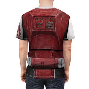 May include: A red and white graphic t-shirt with a detailed battle armor design. The shirt has a crew neck and short sleeves. The design includes rectangular and circular shapes, and a belt-like detail at the waist.