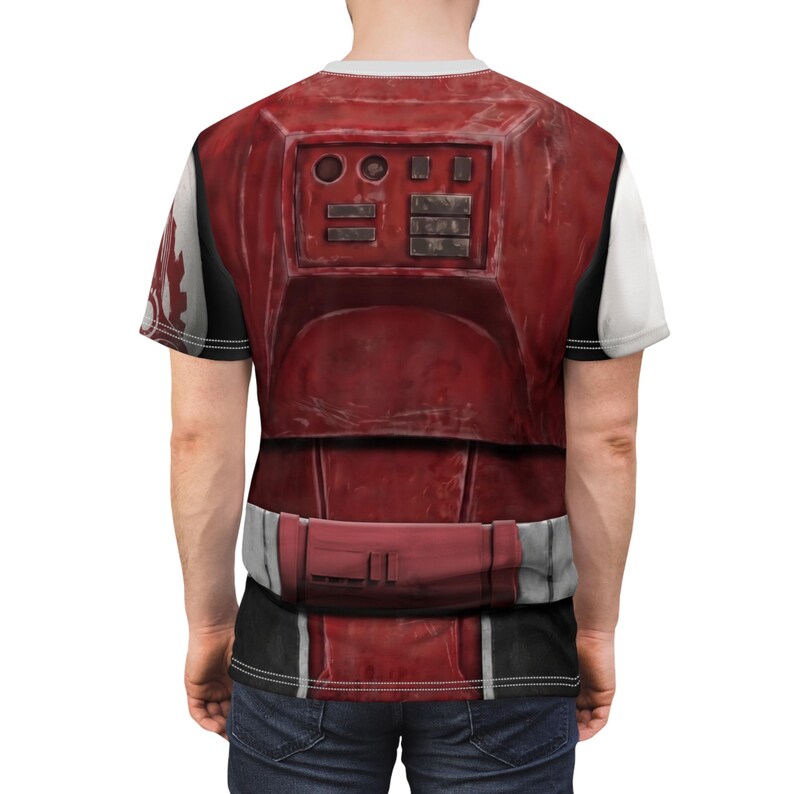 May include: A red and white graphic t-shirt with a detailed battle armor design. The shirt has a crew neck and short sleeves. The design includes rectangular and circular shapes, and a belt-like detail at the waist.