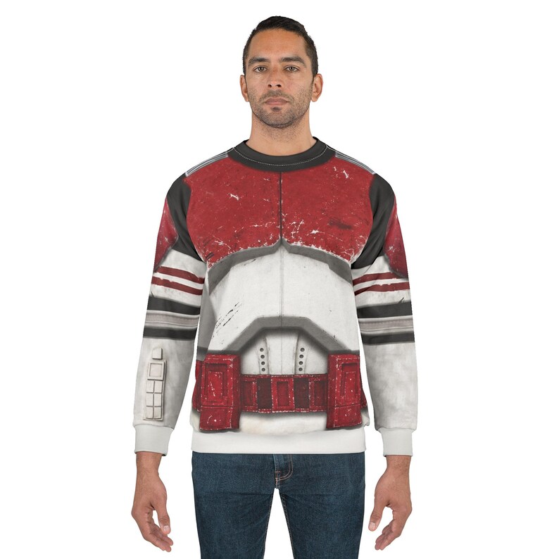 May include: A white, red, and black sweatshirt with a detailed print of clone trooper armour. The long-sleeved top has a crew neck and is worn by a person in blue jeans.