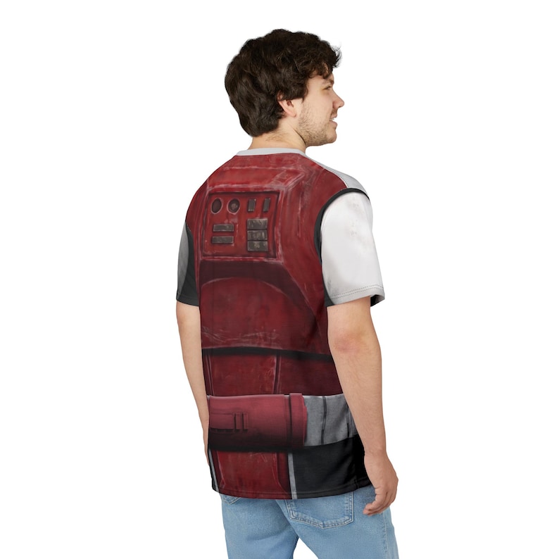May include: A red and grey graphic t-shirt with a detailed armour design. The design includes rectangular panels, buttons, and a belt-like element. The shirt has a white short sleeve and a grey neckline.