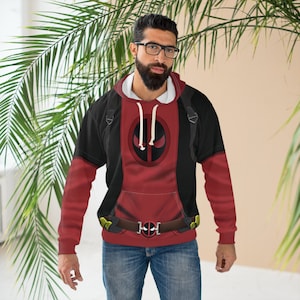 May include: A red and black Deadpool hoodie with a large Deadpool logo on the front. The hoodie has a drawstring hood and a kangaroo pocket. The belt has a Deadpool logo buckle. The person is wearing blue jeans and glasses.