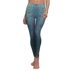 May include: Blue and teal leggings with a scale-like pattern. The leggings feature a high waist and a gradient effect, transitioning from lighter blue at the top to darker teal at the bottom. The design resembles reptile skin.