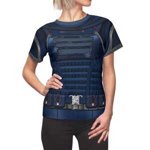 May include: A short-sleeved, blue t-shirt featuring a detailed print of a tactical vest. The design includes a metallic-looking chest plate, vertical ribbed panels, and a belt with a silver buckle. The shirt has a crew neck and a fitted silhouette.