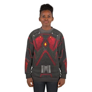 May include: A dark gray sweatshirt with a red and black design resembling armor. The design includes geometric shapes, a belt detail, and a yellow diamond shape. The long-sleeved shirt is worn by a person.