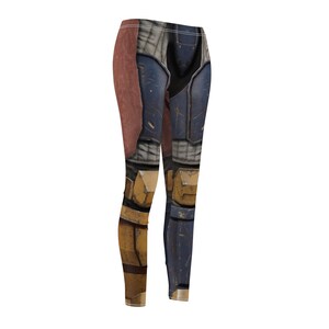 K&ouml;nnte beinhalten: Leggings mit einem Digitaldruck, der einer R&uuml;stung &auml;hnelt. Das Design weist Farbt&ouml;ne von Blau, Braun und Gelb auf und erzeugt ein strukturiertes, metallisches Aussehen. Die Leggings sind figurbetont und wahrscheinlich aus einem dehnbaren Material.