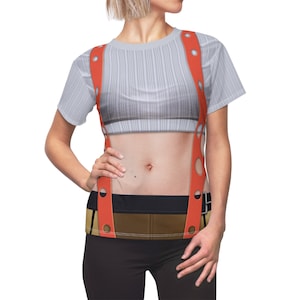 May include: A white short-sleeved shirt with a printed design of a woman's torso wearing suspenders. The suspenders are red with white polka dots and have a brown belt.