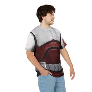 May include: A short-sleeved t-shirt with an armour-like design. The top section is white and grey, the lower section red and grey, with silver details. The person is wearing light blue jeans.