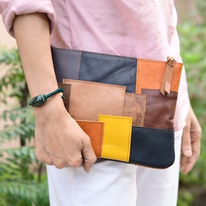 May include: A patchwork leather clutch bag with a variety of colours including brown, orange, yellow, and black. The bag has a zipper closure and a small strap.
