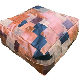 May include: A large, square, patchwork leather ottoman with a variety of brown, tan, and black leather pieces sewn together. The ottoman is made of thick, durable leather and has a slightly distressed look.