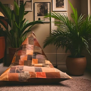 May include: A large, triangular beanbag chair with a patchwork design in shades of brown, orange, and tan. The chair is placed on a light brown rug, with potted plants in the background. The beanbag is a unique piece of furniture.
