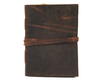 May include: A dark brown leather journal with a wrap-around leather strap. The journal has a distressed appearance, with variations in color and texture. The pages are visible at the top, and the binding is stitched. A classic and rustic notebook.
