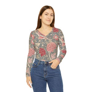 May include: A long-sleeved V-neck top with a floral pattern in shades of pink, red, and blue. The top is paired with blue denim jeans. The floral design covers the entire top, including the sleeves.